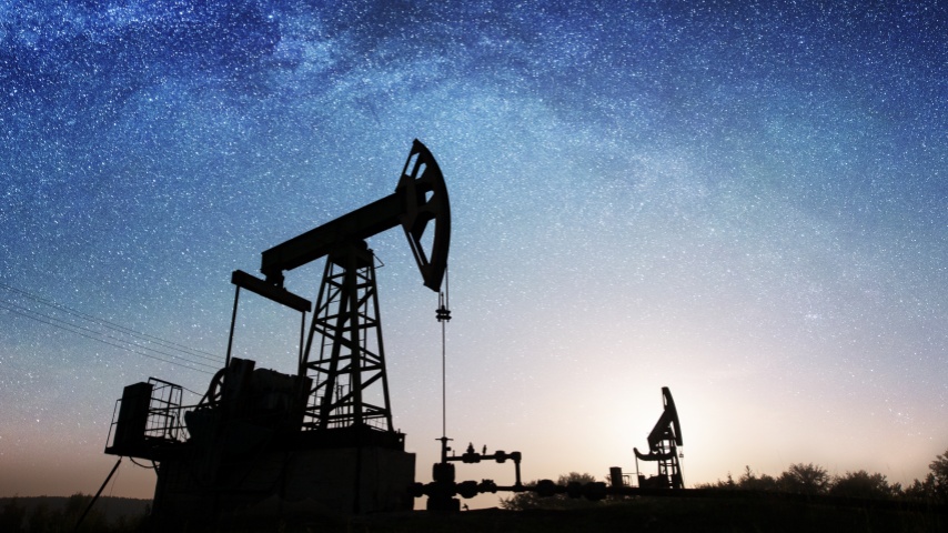 Silhouette of two oil pumps are pumping crude oil on the oil field under night sky with stars and Milky way. Oil industry equipment